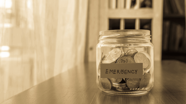 A glass jar labeled "EMERGENCY" filled with coins, representing Financial Literacy and the importance of building an emergency fund.