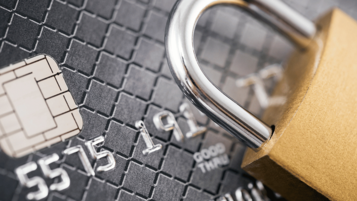 Close-up of a black credit card with an EMV chip, partially covered by a metallic padlock, symbolizing credit card security.