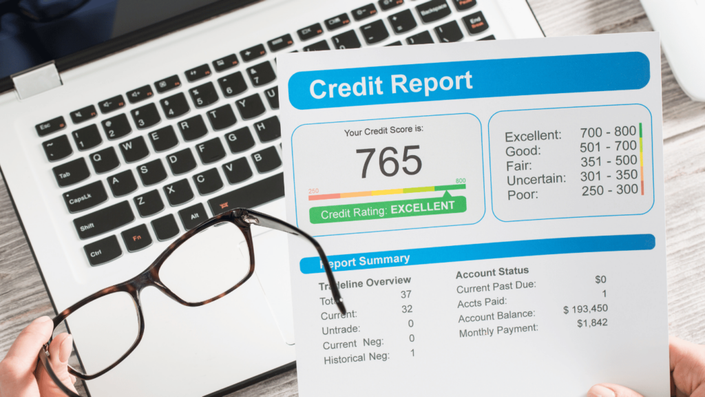 Close-up view of a credit report document showing an excellent credit score of 765 next to a laptop and glasses.