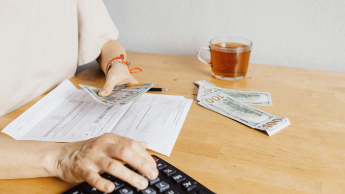 A person counting $100 bills while using a calculator, with utility bill documents on the table, symbolizing the management of Utility Costs.